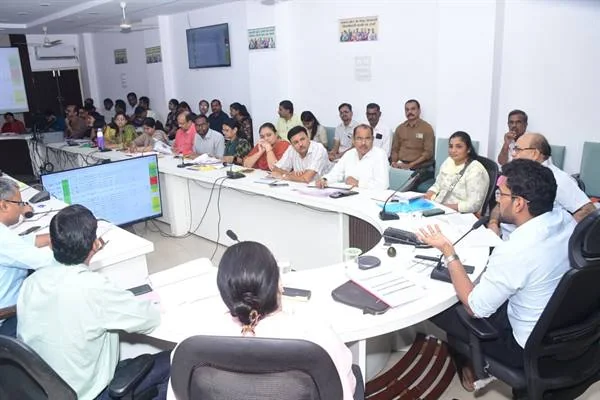 सभाकक्ष में यू आकार की मेज के चारों ओर बैठे अधिकारी बैठक में चर्चा करते हुए